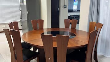 A dining area with a round table and eight chairs, a refrigerator, and a television in the background.