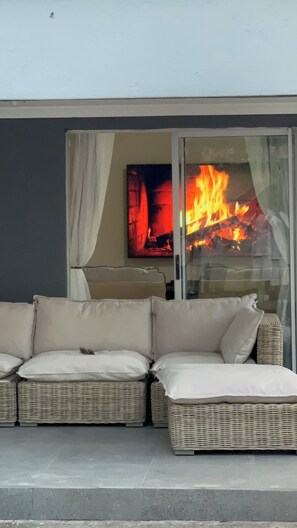 Un sofá de mimbre con cojines, un vidrio y un fuego ardiendo en su interior.