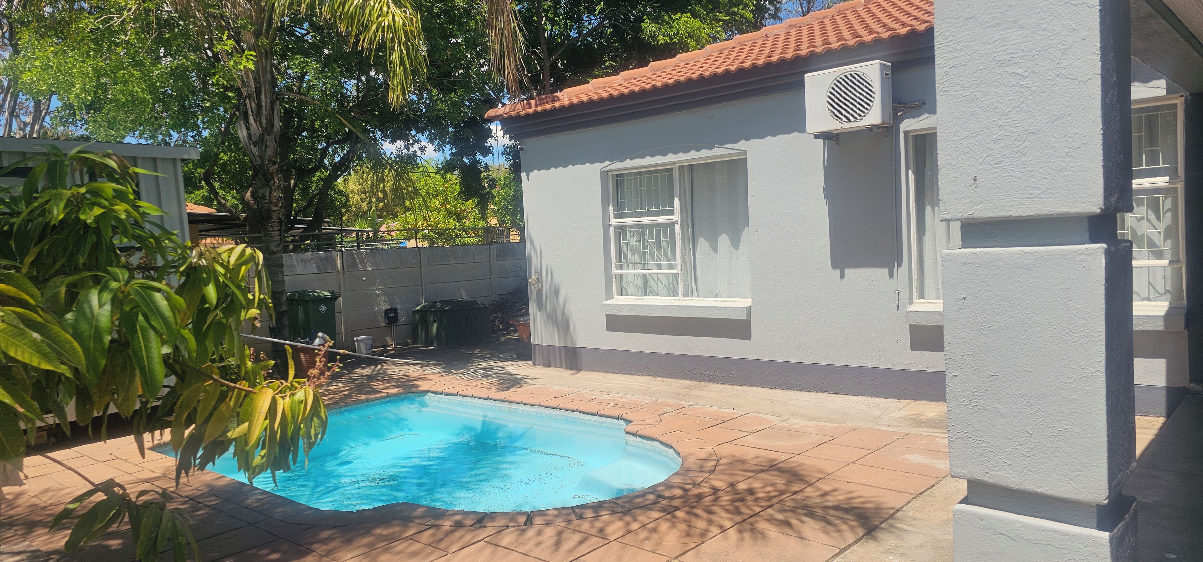 A residential property with a swimming pool, a tiled patio, and a house with a red-tiled roof.