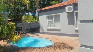 A residential property with a swimming pool, a tiled patio, and a house with a red-tiled roof.