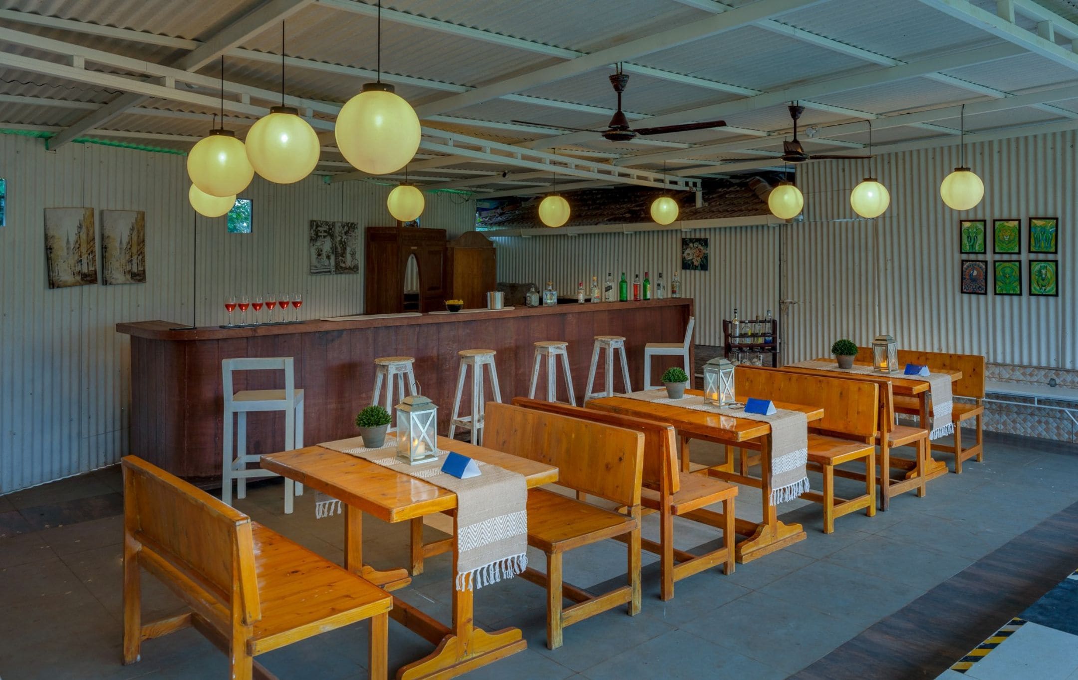 Interior de restaurante con mesas y sillas de madera, una zona de bar y lámparas esféricas colgantes.