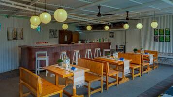 Interior de restaurante con mesas y sillas de madera, una zona de bar y lámparas esféricas colgantes.