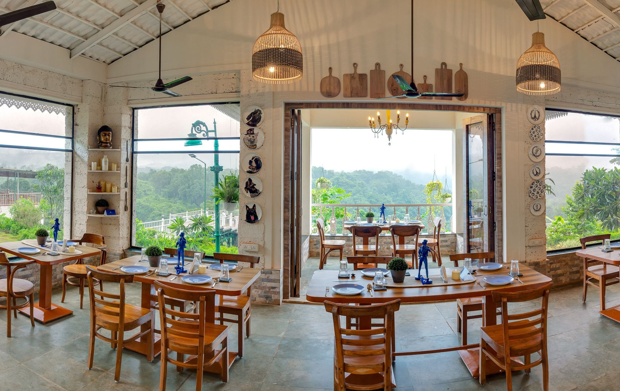 Un restaurante con varias mesas y sillas, amplias ventanas con vistas a zonas verdes y elementos decorativos en la pared.