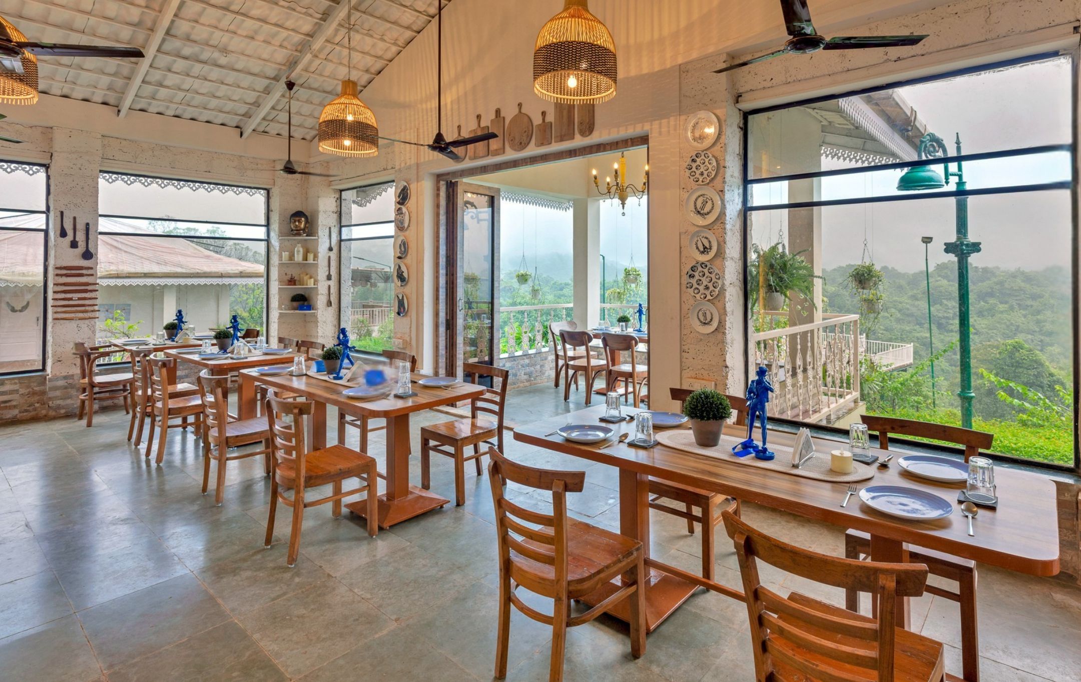 Un vaste espace dédié à la salle à manger, avec de nombreuses tables et chaises en bois, de grandes fenêtres donnant sur l’extérieur et des luminaires suspendus.