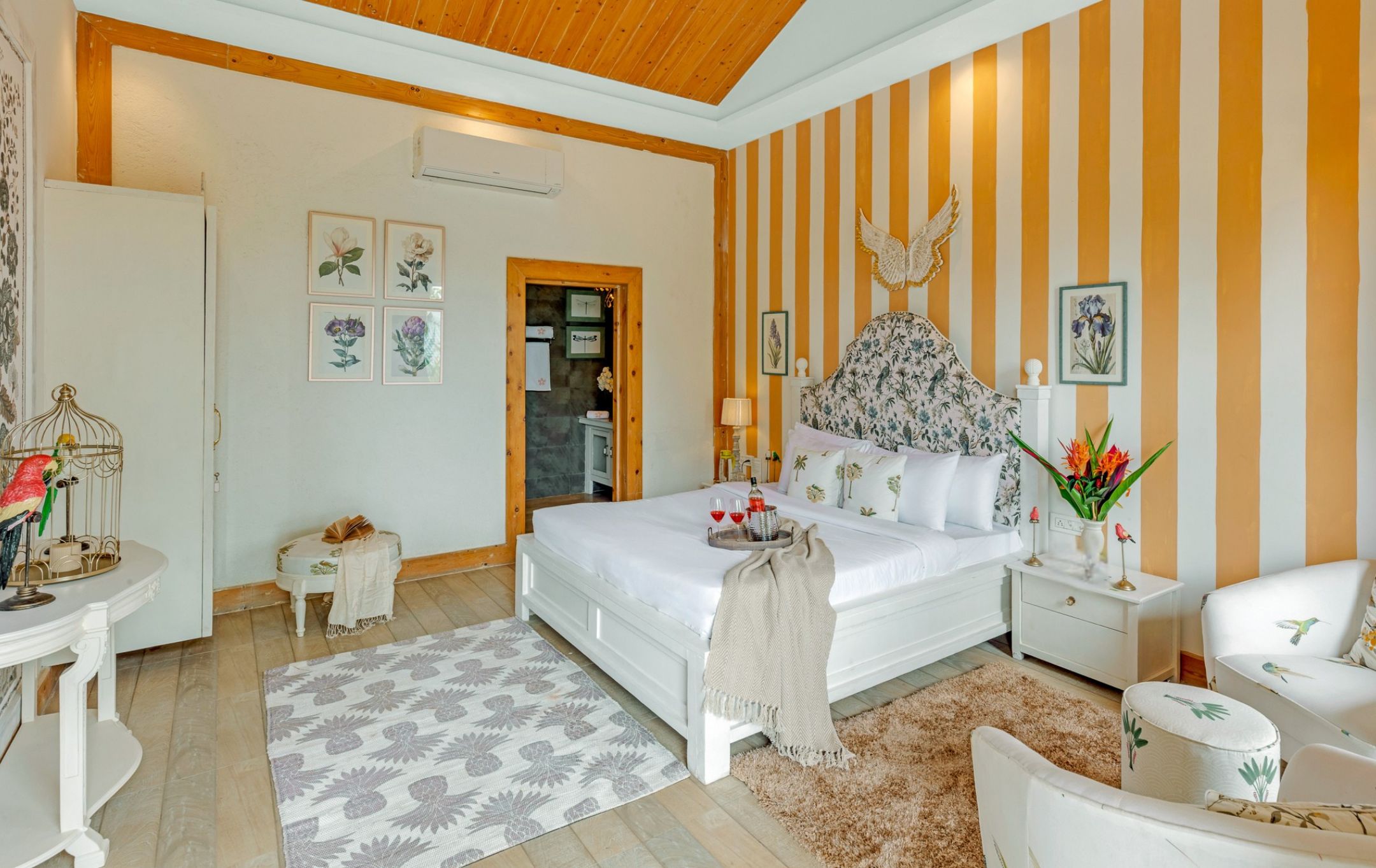 A bedroom with a bed, bedside tables, a nightstand, a chair, a small table, and a birdcage.