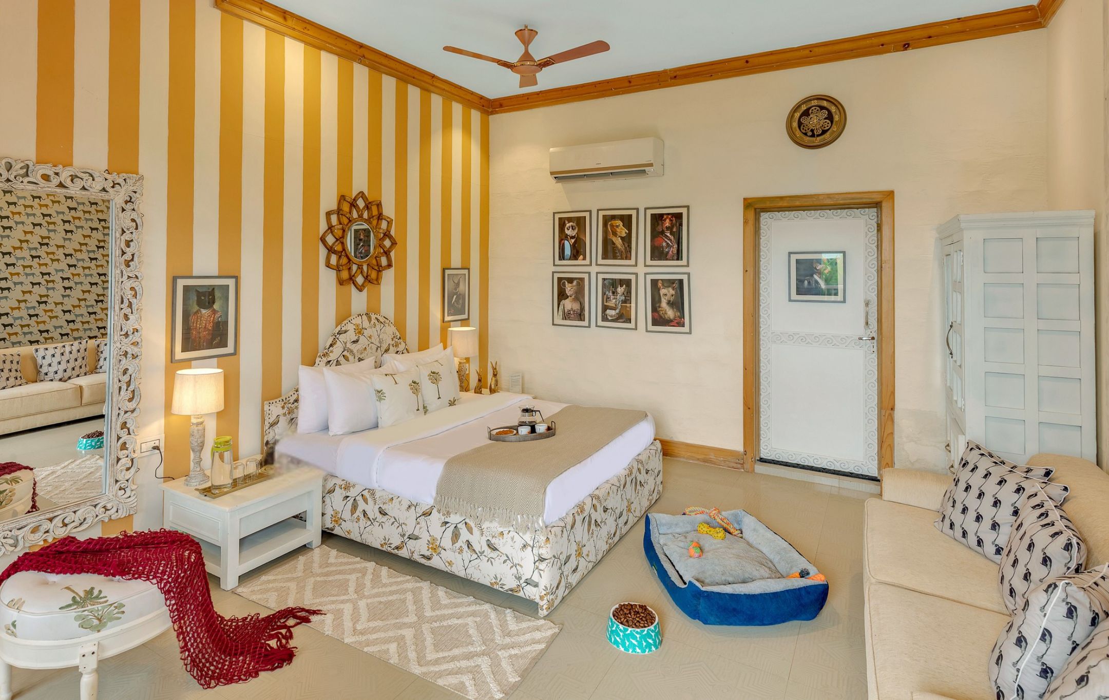 A hotel room with a bed, a sofa, a small table, a mirror, a ceiling fan, and a door.