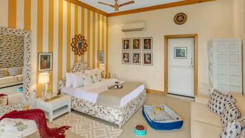 A hotel room with a bed, a sofa, a small table, a mirror, a ceiling fan, and a door.