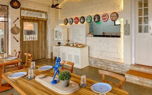 A dining area with wooden tables and chairs, a white counter with a menu, and a wall decorated with various beverage bottle caps. - ELIVAAS Signature Junglebrooke  Cottage (Vitthalwadi)