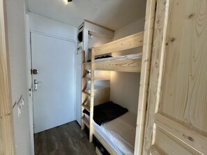 Ein kleines Zimmer mit Etagenbett, Kleiderschrank und Schreibtisch mit Lampe.