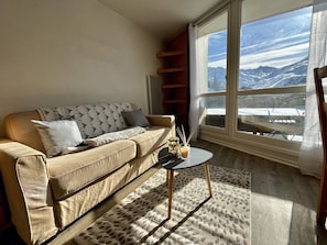Ein Wohnzimmer mit einer Couch, einem kleinen Tisch und Blick auf schneebedeckte Berge durch große Fenster.