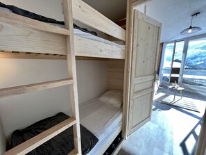 A bunk bed with a wooden frame, a small table with a drink, and a view of a snowy landscape through large windows. - Estrella - Les 3 Vallées - Les Ménuires (Les Menuires)