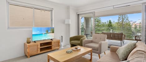 A modern living room with a flat-screen TV, wooden entertainment unit, sofa, and a balcony with outdoor furniture.