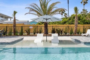 Une piscine entourée d’une clôture en bois, avec des chaises longues blanches et un palmier.