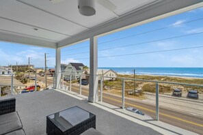 Un balcon avec vue sur la plage et l’océan, comprenant une table en verre et des chaises en osier.