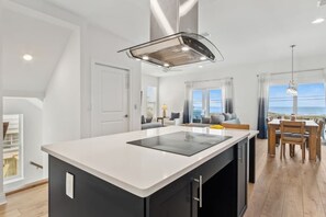 Eine moderne Küche mit einer zentralen Kochinsel, ein Essbereich mit Tisch und Stühlen sowie Meerblick durch große Fenster.