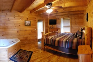 Ein Schlafzimmer in einer Blockhütte mit einem hölzernen Bett, einem großen Fenster, einem Deckenventilator und einer Badewanne.