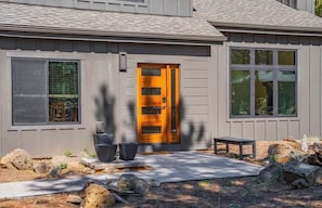 Une maison moderne avec une porte d’entrée en bois, une fenêtre et un petit espace extérieur aménagé pour s’asseoir.
