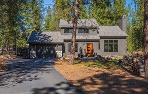 A two-story house with a stone foundation, a grey roof, and a front entrance with a wooden door. - Lark & Leisure (Bend)