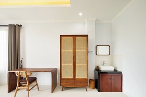 Ein Zimmer mit einem Holztisch, einem Korbstuhl, einem Kleiderschrank, einem Spiegel und einem Waschbecken.