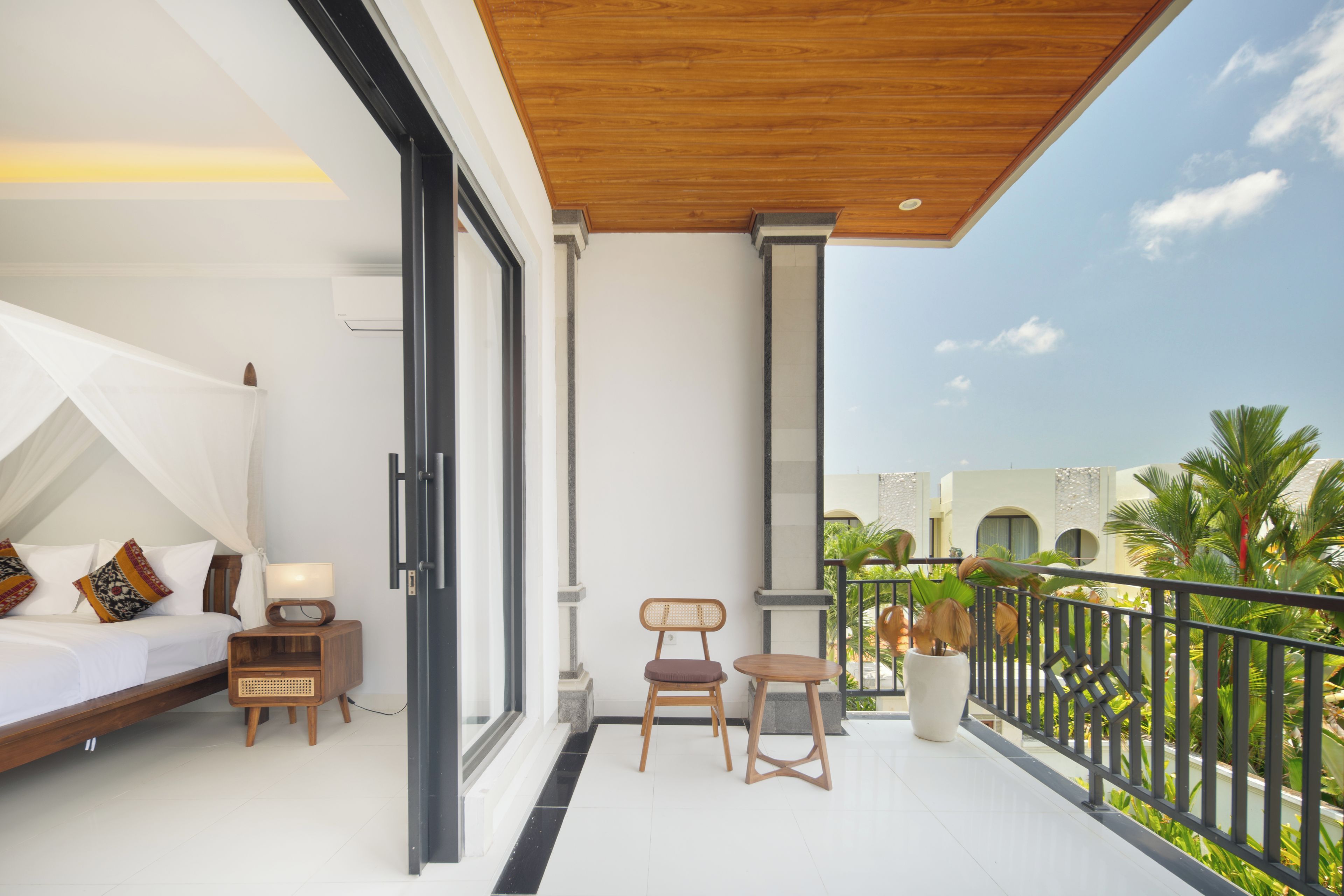 A balcony with a bed, a nightstand, a chair, and a potted plant.