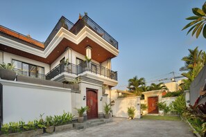 A two-story residential building with a balcony, a wooden door, and a concrete driveway. - Canggu Nadi Villa (Badung)
