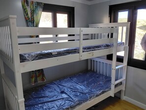 A bunk bed with a lower bunk covered in plastic, a window with curtains, and a view of the outdoors.