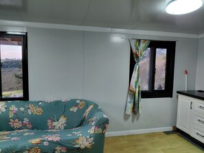 A room with a bed, a window with a curtain, a cabinet, and a view of a landscape.