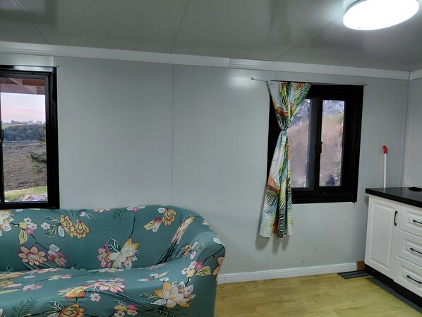 A room with a bed, a window with a curtain, a cabinet, and a view of a landscape.