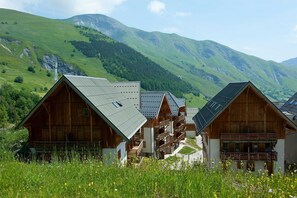 Eine Reihe von Holzhäuschen mit schrägen Dächern, vor einer Kulisse aus grünen Hügeln und Bergen.