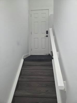 A narrow staircase with a dark wooden floor leading to a white door. - Cozy 2-bedroom basement apartment (Calgary)
