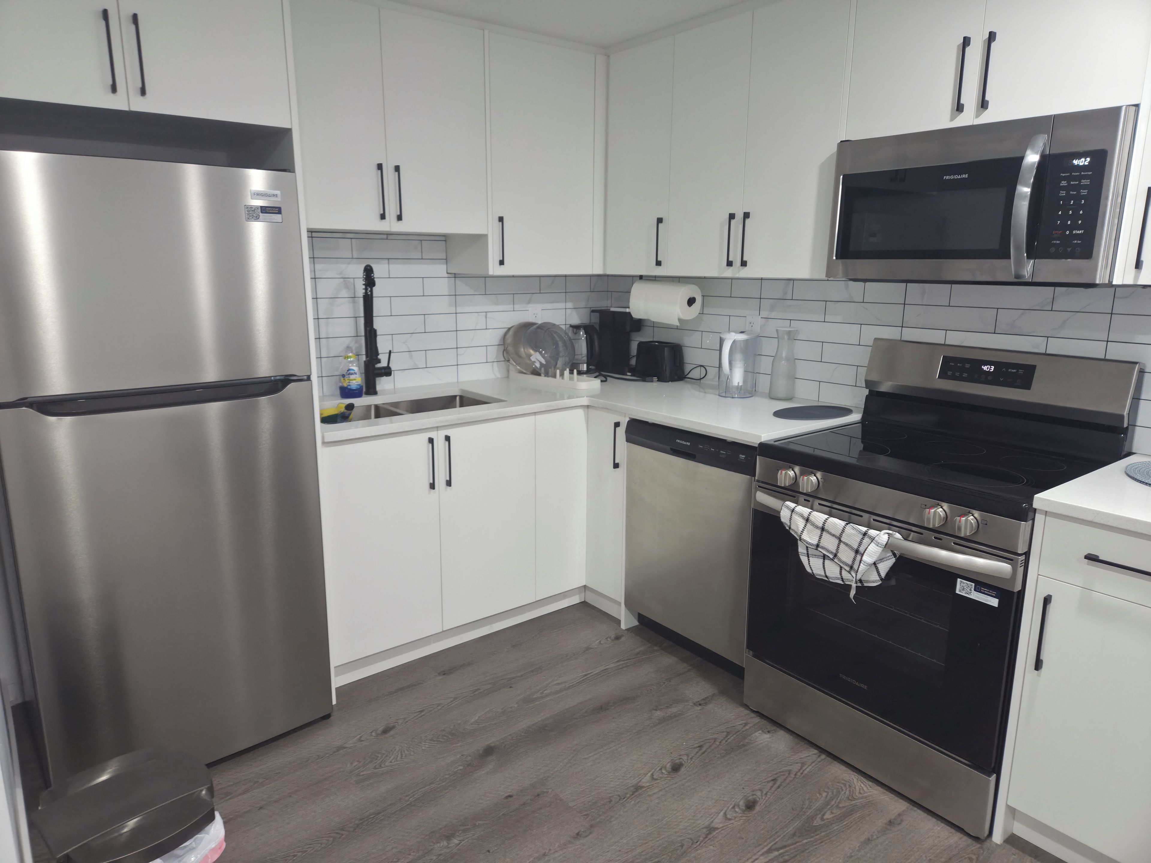 A modern kitchen with stainless steel appliances, white cabinetry, and a wood floor.