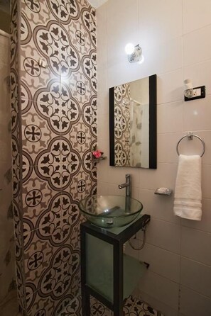 Un baño con papel tapiz estampado, un lavabo de vidrio, un espejo y un perchero para toallas.