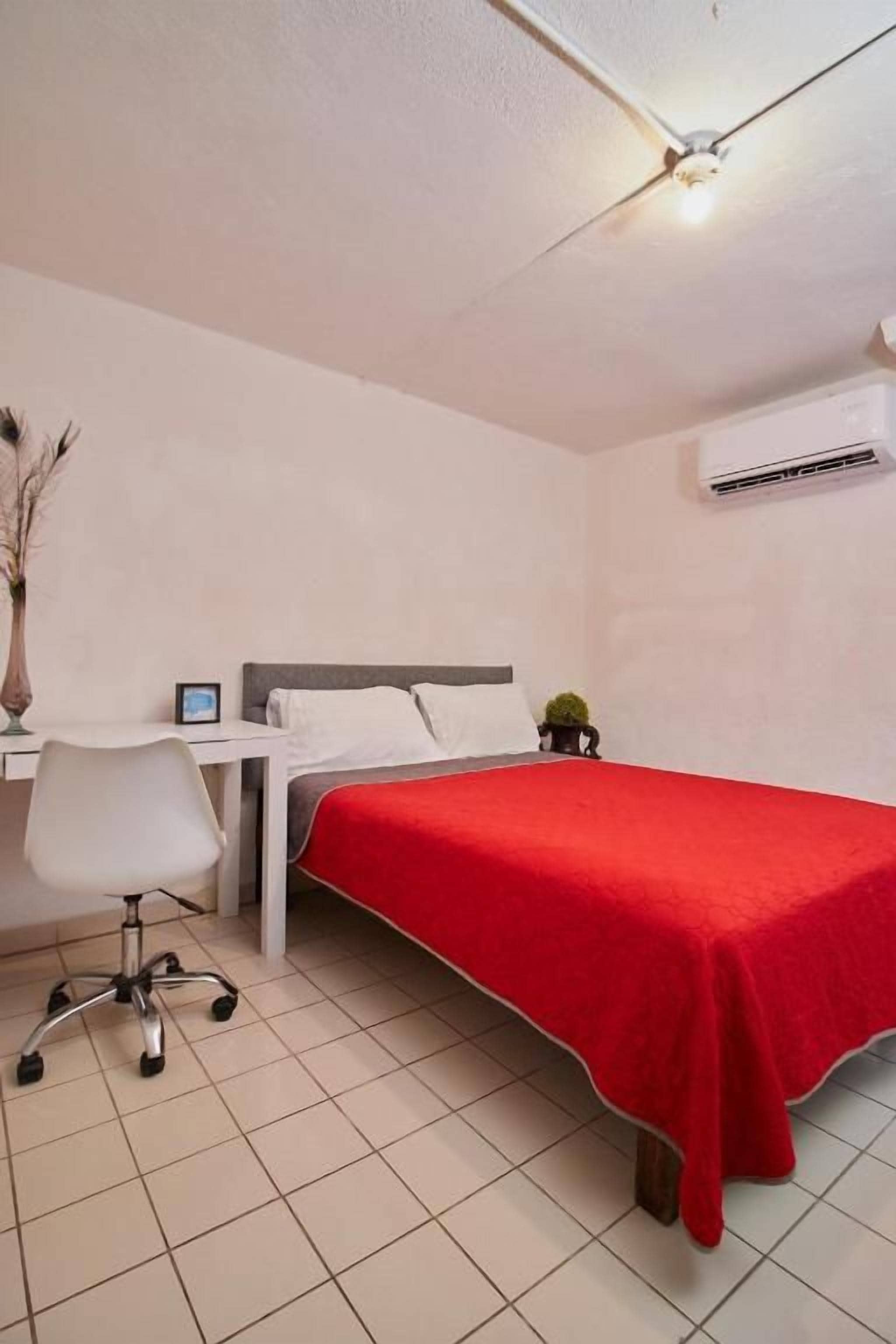 A bedroom with a bed, a desk, a chair, and an air conditioning unit.