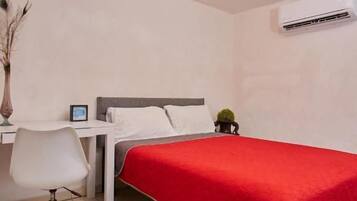 A bedroom with a bed, a desk, a chair, and an air conditioning unit.