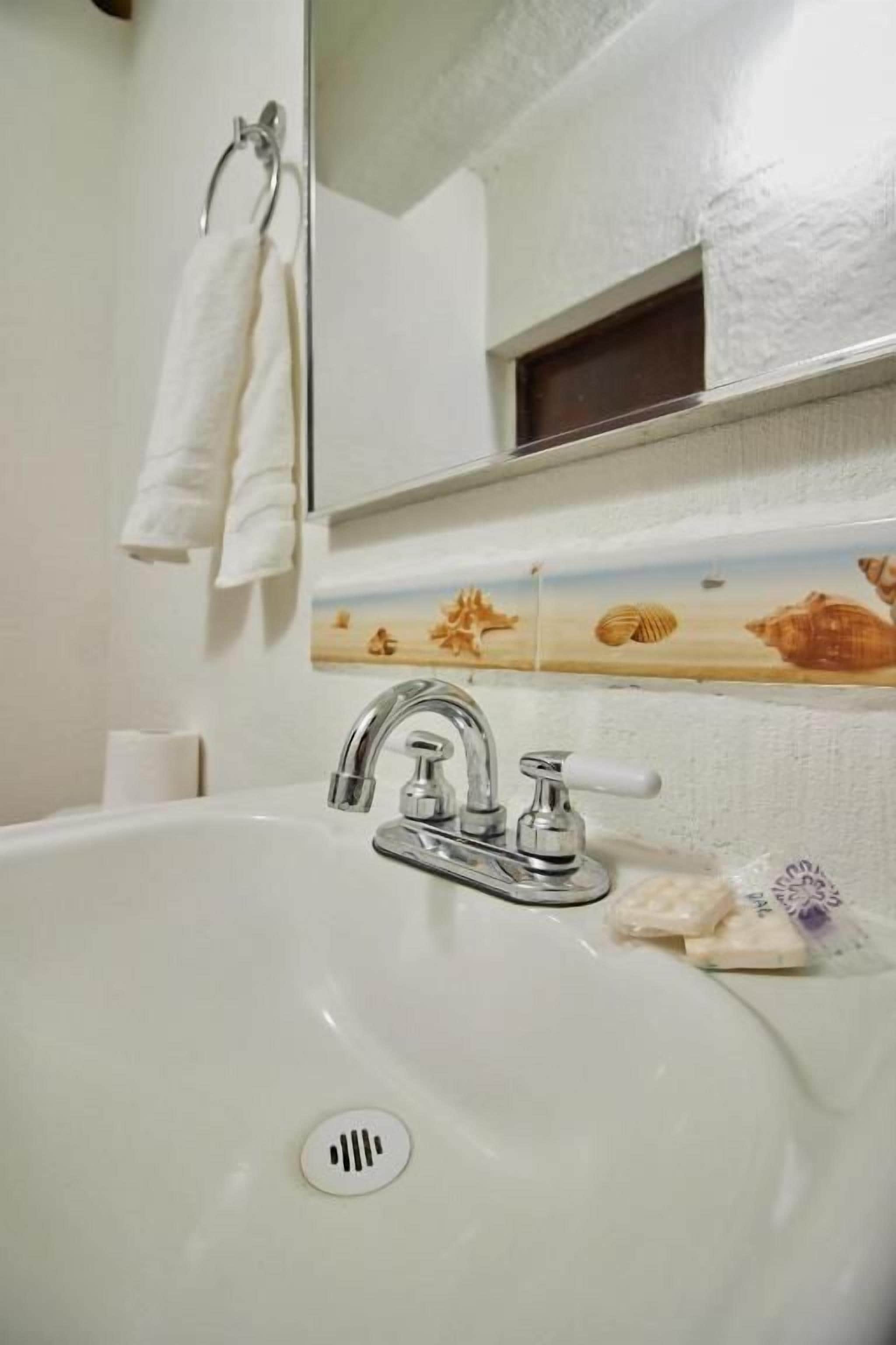Un baño con lavamanos blanco, espejo y toallero.