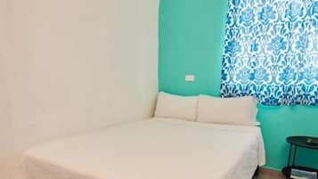 Una habitación con cama, una ventana con cortinas estampadas y una mesita con una revista.