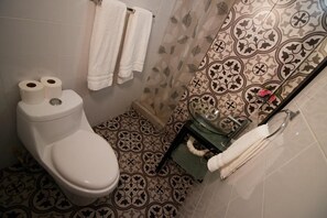Un baño con inodoro, dos rollos de papel higiénico, lavamanos de vidrio y azulejos con diseño.