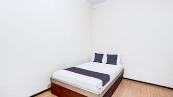 A small, single-bed room with a wooden headboard, white bedding, and a dark-colored bed runner.