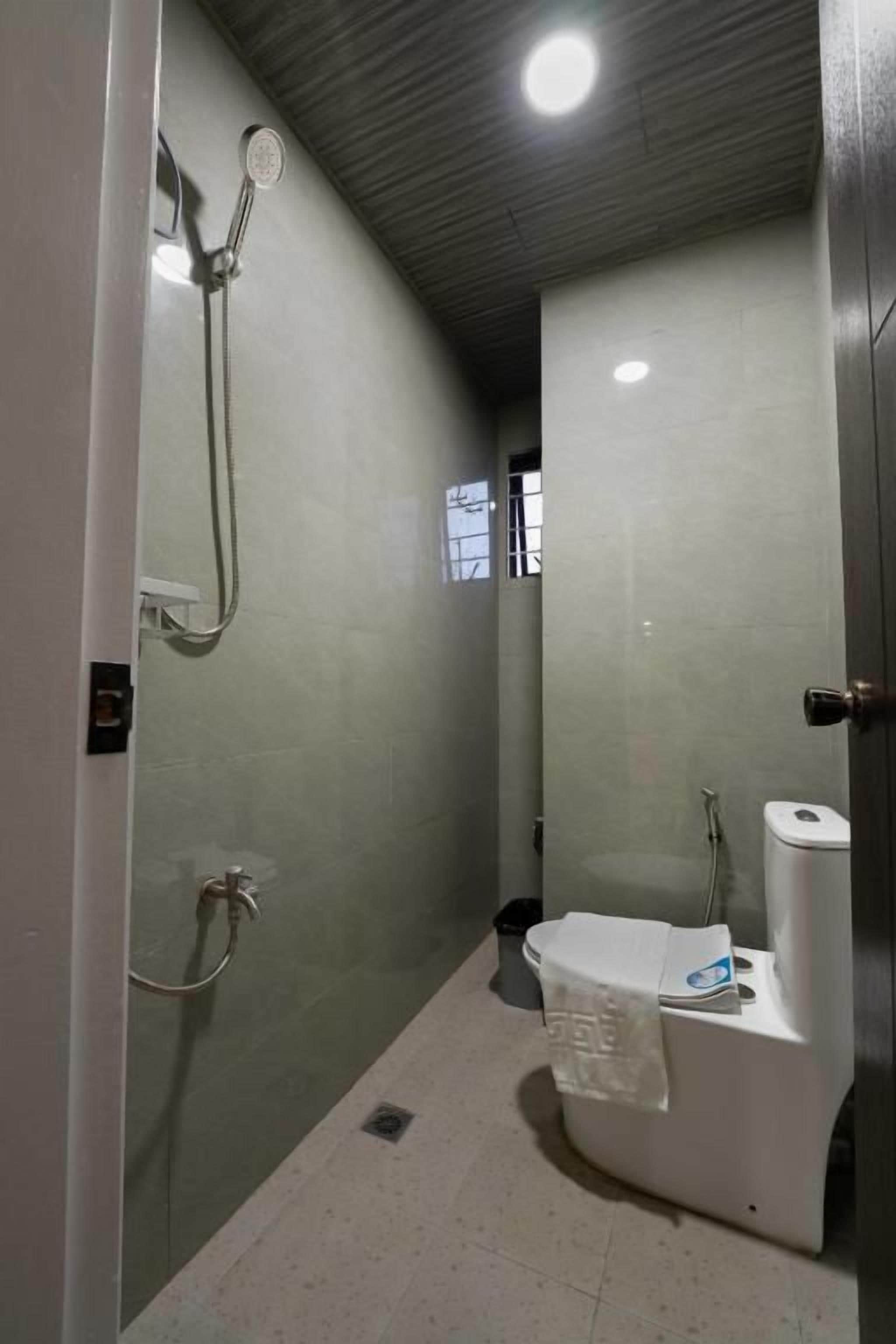 A small, enclosed bathroom with a toilet, a shower, and a towel hanging on the wall.