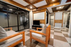 Uma sala de estar moderna com piso xadrez, móveis de madeira, uma televisão de tela plana e uma porta de vidro que dá para uma escada.