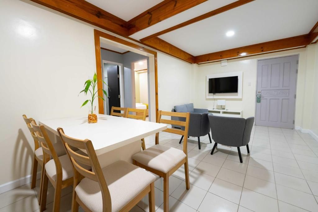 Un coin repas avec une table blanche et des chaises en bois, un canapé gris et un téléviseur fixé au mur.