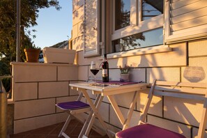 A small outdoor seating area with a table and two chairs, a bottle of wine, and a glass on the table. - Apartments Lovro - Duplex One Bedroom Apartment With Terrace and Partial Sea View (Dubrovnik)