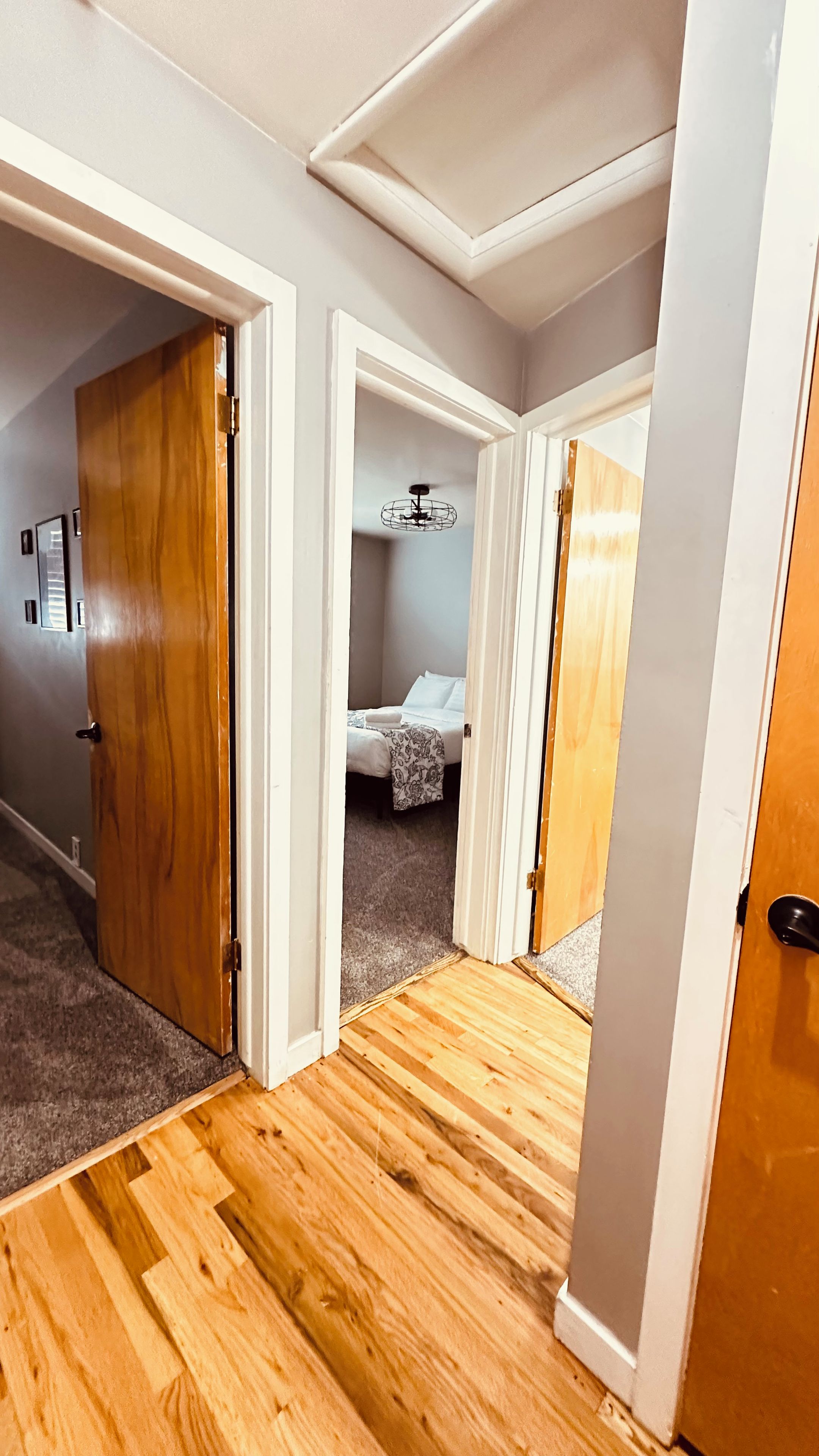 A hallway with wooden flooring, white walls, and a bed with a white duvet in the background.