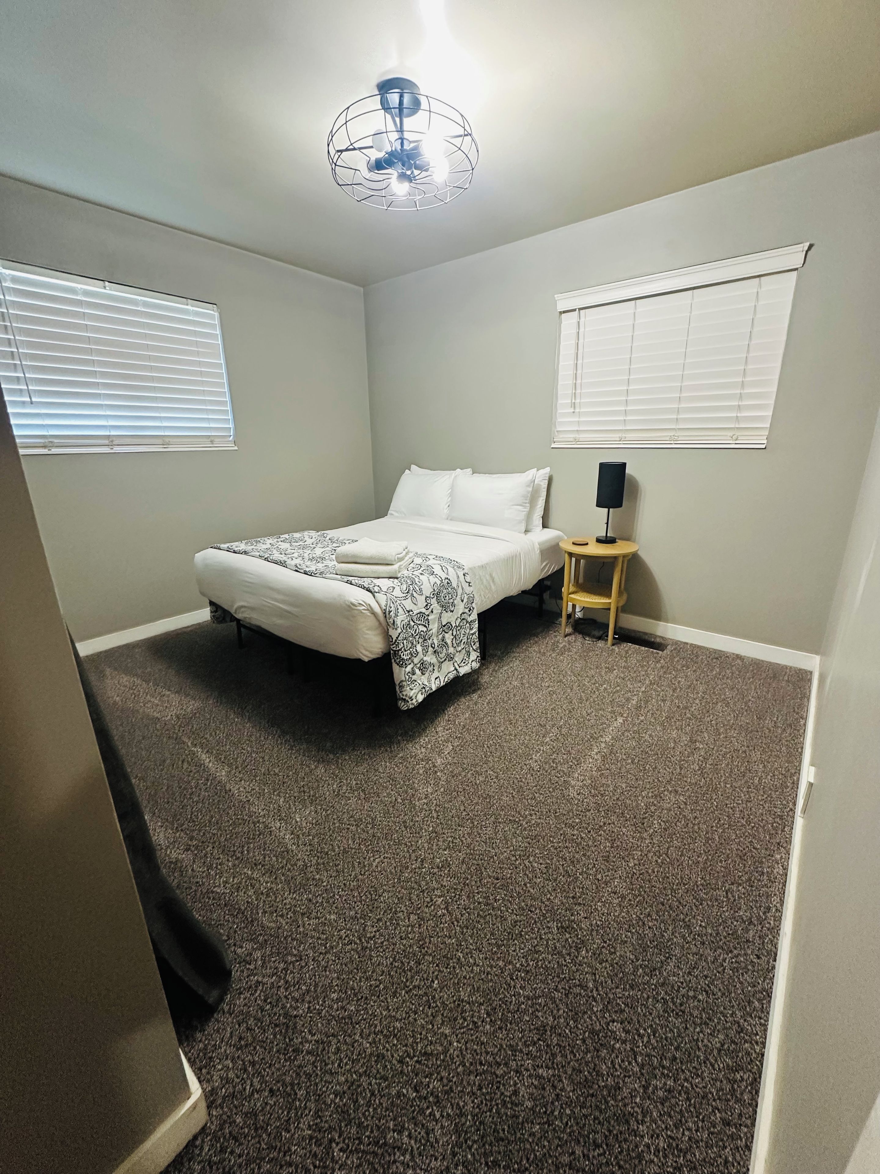 A bedroom with a bed, a bedside table with a lamp, and a ceiling fan.