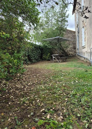 Ein Garten mit Picknicktisch und Sonnenschirm, umgeben von dichtem Grün und einer Steinmauer.
