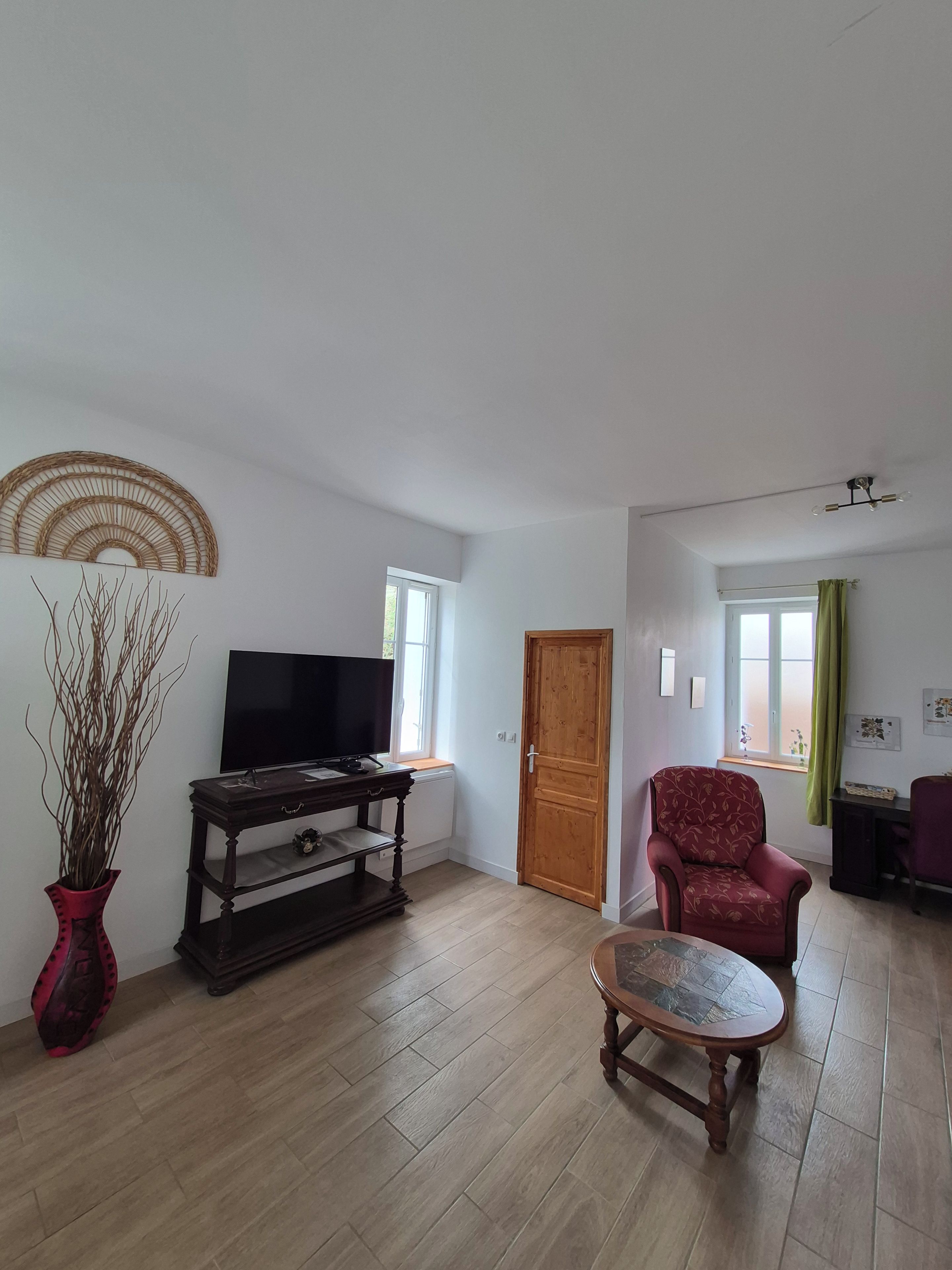 A living room with a television, a wooden cabinet, a red armchair, and a wooden floor.