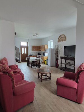 A living room with red sofas, a coffee table, and a TV. There is a kitchen in the background with wooden cabinets and a dining area. - An 80-square-meter house halfway between Puy-du-Fou and Futuroscope (Val en Vignes)
