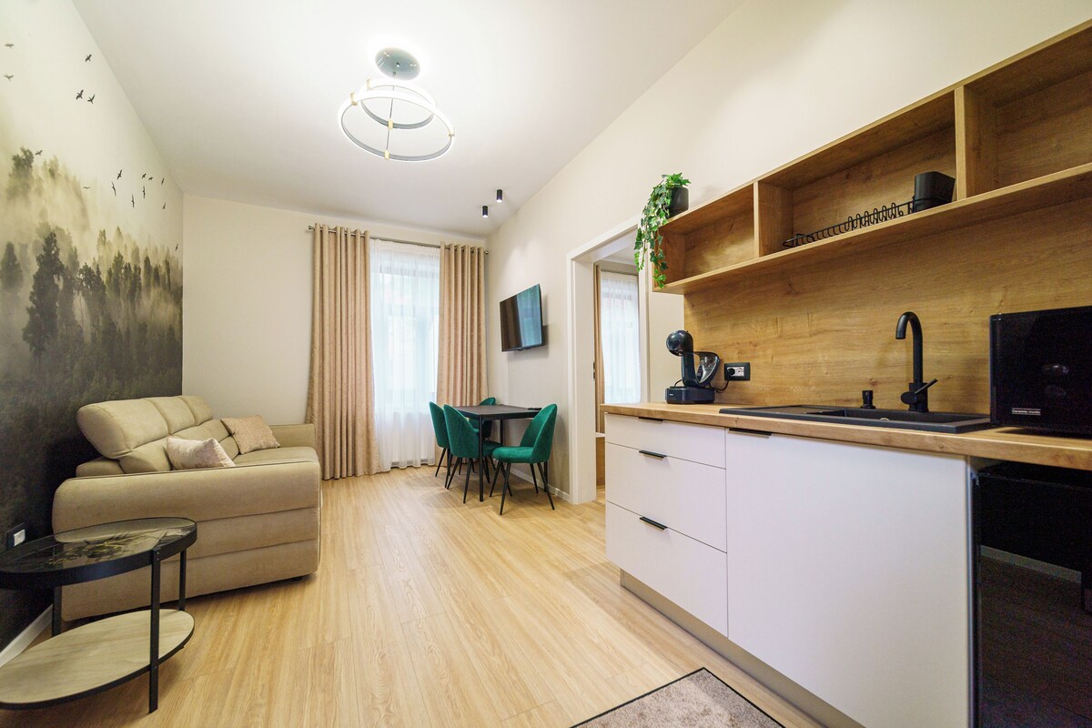 Uma sala de estar moderna com sofá, canto de jantar com cadeiras, cozinha com pia e televisão, e piso de madeira.