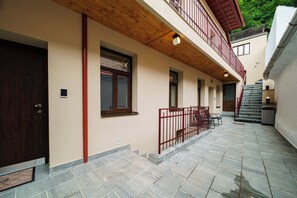 Um edifício com fachada de madeira, varanda e pátio com piso de pedra.