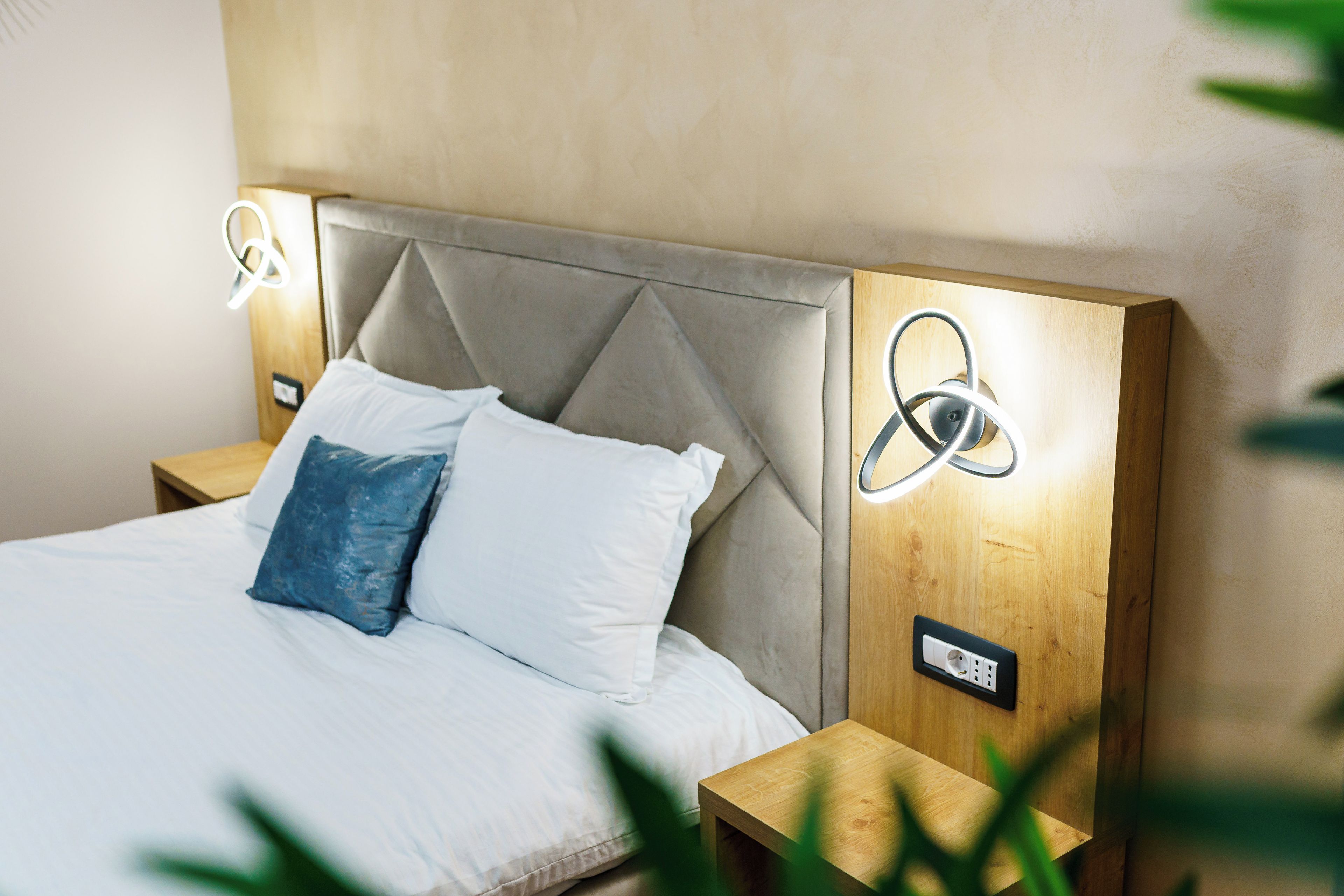 Una cama con cabecera, dos mesitas de noche e iluminación instalada en la pared.
